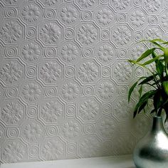 a green plant in a silver vase sitting on a white shelf next to a wall