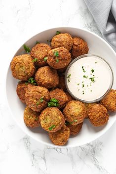 a white bowl filled with fried meatballs next to a small cup of ranch dressing