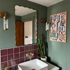 a bathroom sink sitting under a mirror next to a potted plant