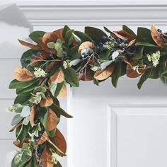 a wreath with leaves and flowers hanging on the front door frame, ready to be decorated for christmas