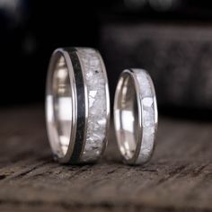 two wedding bands with white marble inlays are on top of a wooden table