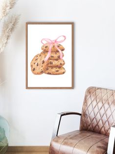 a painting of cookies tied with a pink ribbon on a white wall next to a brown leather chair