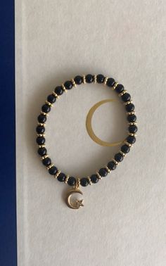 Black and gold beads on elastic string with a gold moon and star charm. Cheap Gold Beaded Bracelets With Black Beads, Spiritual Black Beaded Charm Bracelet, Spiritual Gold Beaded Bracelet With Black Beads, Adjustable Black Bracelet With Star Charm, Black Bracelets With Star Charm As Gift, Gold Bracelets With Star Charm And Round Beads, Black And Gold Bracelet, Black Bracelet Ideas, Gold Moon