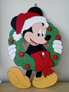 a mickey mouse christmas ornament with a wreath on it's face and ears