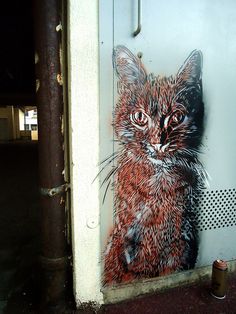 a painting of a cat on the side of a building next to a trash can