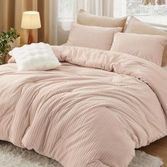 a bed with pink comforter and pillows in front of a white rug on the floor