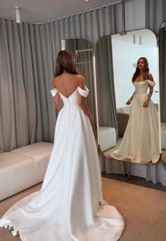 a woman in a white dress is looking at herself in the mirror and she has her back turned to the camera