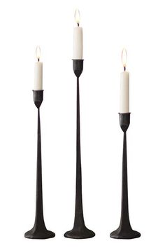 three black candlesticks with one white candle