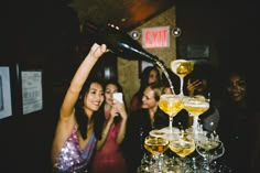 two women are pouring champagne into glasses on a bar while another woman is taking a photo with her cell phone