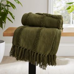 a green blanket sitting on top of a wooden bench next to a potted plant