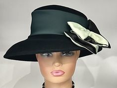 "The featured hat is a  black colored wool winter dress hat.   It has a wide silk band in a forest green color. A gorgeous two tone  bow in black and sage green is placed on an angle. This bow is elegant and classy. The combination of different textures and colors is what makes this hat so charming and disarming. The softness of the bow on the solid black hat is a striking look! This hat can be worn as a winter Church Hat, a Wedding Party Hat, a Tea Party hat,  a Downton Abbey  hat,  winter hat Elegant Black Cloche Hat With Flat Brim, Formal Black Winter Top Hat, Black Winter Cloche Hat For Party, Black Cloche Hat For Evening In Winter, Fitted Black Cloche Hat For Church, Black Cloche Hat For Winter Party, Black Winter Party Cloche Hat, Black Winter Cloche Hat For Evenings, Formal Black Cloche Hat For Winter