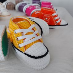 several pairs of crocheted sneakers are lined up on a white surface, all in different colors