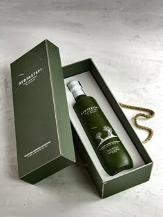 an empty bottle in a green box on a white surface with a gold chain next to it