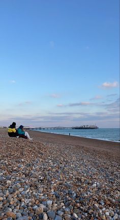 two people sitting on the beach looking out at the water