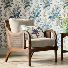 a wooden chair sitting next to a table with a vase on it and a wall paper behind it