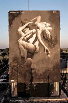 a large painting on the side of a building with two naked people hugging each other