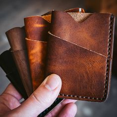 a hand holding three brown leather wallets