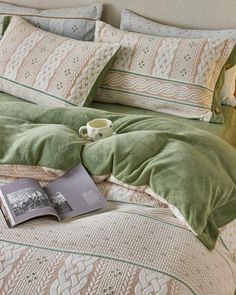 an open book and cup on a bed with green comforter set in the corner