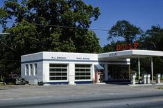 an old gas station sits empty on the side of the road in front of some trees