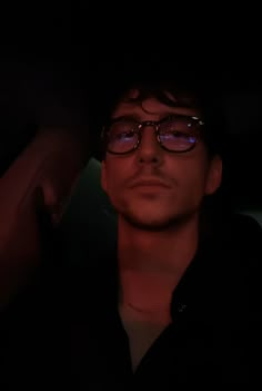 a man wearing glasses is sitting in the dark