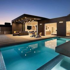 a large swimming pool in front of a modern house at night with the lights on