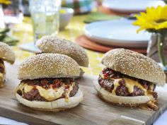 four cheeseburger sandwiches sitting on top of a wooden cutting board next to flowers