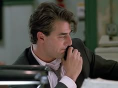 a man sitting at a desk talking on a cell phone while wearing a suit and tie