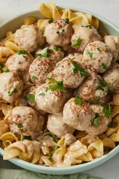 a bowl filled with pasta and meatballs covered in gravy, garnished with parsley