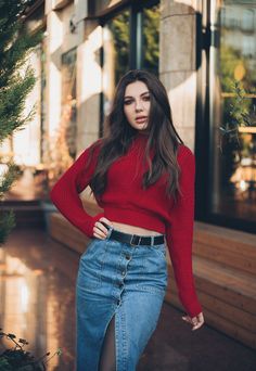 a woman in a red sweater and jean skirt posing for the camera with her hands on her hips