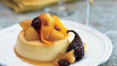 a white plate topped with fruit covered dessert next to a glass of wine on top of a table