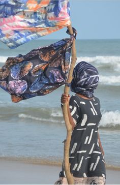 a woman is standing on the beach with her scarf draped over her head and looking at the ocean