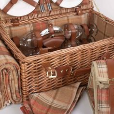 a wicker picnic basket with plates and utensils in it next to a plaid bag