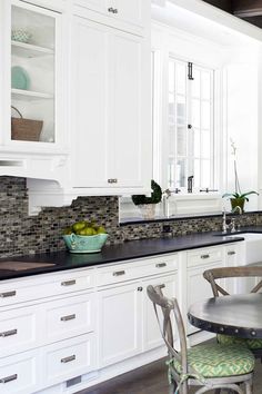 a kitchen with white cabinets, black counter tops and green accents on the backsplash