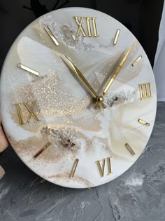 a white clock with gold roman numerals on it's face and hands