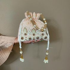 This Pearl and Zirconia and Sequin studded Peach Potli is a beautifully handcrafted Indian Batwa Bag, perfect for adding a touch of traditional elegance to any occasion. The bag features a stunning peach base adorned with intricate pearl embroidery, creating a luxurious and festive appeal. The shimmering sequins add a glamorous flair, making it an ideal accessory for brides or wedding guests. ✅ How To Order Please select your color in option. ✅ SPECIFICATIONS: ⦿  Available in 3 colors : Hot pink, Baby blue, Peach  ⦿ Dimension: Length 9", Width 9" ⦿ Item Type: Indian Potli Bag ⦿ Material: Fabric, Sequins, Zardosi, Etc. ⦿ Gender: Women ✅ FEATURES: ⦿ Made using beads and sequins and rhinestones on silk fabric ⦿ Ethnic and contemporary ⦿ Has a drawstring closure ⦿ Add a touch of glamour ⦿ Plea Festive Embroidered Beige Potli Bag, Embroidered Pouch For Reception, Embroidered Rectangular Potli Bag For Wedding, Festive Embroidered Pouch For Reception, Pink Zari Work Bag For Reception, Embroidered Festive Wedding Bags, Embroidered Wedding Bag For Festive Season, Festive Cream Bag With Pearl Embroidery, Festive Embroidered Wedding Bags