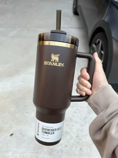 a person holding a coffee cup in front of a car with the word stanley on it