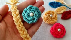 someone is holding three different colored crochet flowers in their hand, one has a pearl bead on it