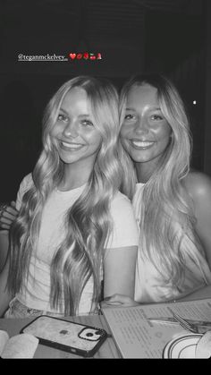 two beautiful young women sitting next to each other at a table in front of a menu