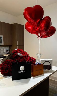 red roses and balloons are sitting on a counter in front of a chanel bag