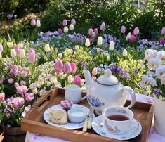 there is a tray with tea and cookies on it in the middle of some flowers