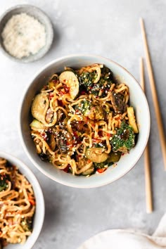 two bowls filled with noodles and vegetables next to chopsticks