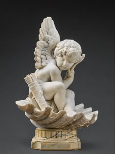 a statue of an angel sitting on top of a wave holding a brush and book