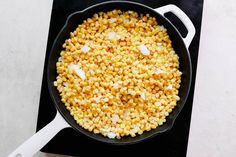 corn is being cooked in a skillet on the stove top with a spatula