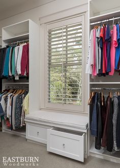 an organized closet with clothes hanging on rails and drawers, along with a bench in front of the window