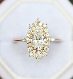 an engagement ring with a diamond center surrounded by smaller diamonds on a white cloth box