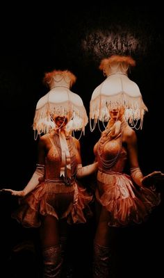 two women dressed in costumes standing next to each other with lamps on their heads and hands