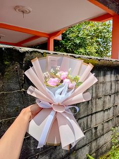 a hand holding a bouquet of flowers on top of a stone wall next to a brick wall