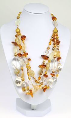 Earth tones come alive in the exquisite design of the Amber Citrine Crystal Quartz Beaded Gemstone Necklace. This luxurious handmade necklace features a multi-strand design that fills out the neckline and complements rounded and plunging styles to perfection. The design combines smooth crystal quartz and orange citrine beads with chunky of golden amber and freshwater pearls that are gold in tone. For a sleek finishing touch, hammered fine silver beads are mixed in, bringing a cool tone to the ot Luxury Amber Natural Stones Beads And Cabochons, Luxury Vintage Amber Beaded Necklaces, Luxury Amber Crystal Necklace, Elegant Style, Luxury Elegant Amber Crystal Necklaces, Elegant Beaded Glass Crystal Necklace, Elegant Multi-strand Crystal Necklaces With Polished Beads, Elegant Multi-strand Crystal Necklace With Polished Beads, Elegant Beaded Crystal Necklace With Oval Beads, Elegant Multi-strand Glass Beaded Necklaces