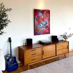 a living room with a couch, guitar and painting on the wall above it's entertainment center