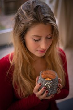 a woman holding a candle in her hand and looking down at the bowl she is holding